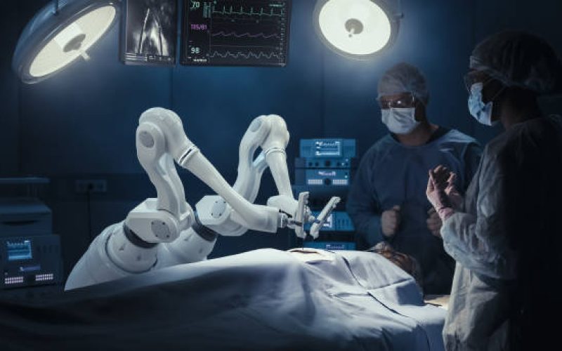 Two Surgeons Observing High-Precision Programmable Automated Robot Arms Operating Patient In High-Tech Hospital. Robotic Limbs Performing Complex Nanosurgery, Doctors Looking At Vitals On Monitor.